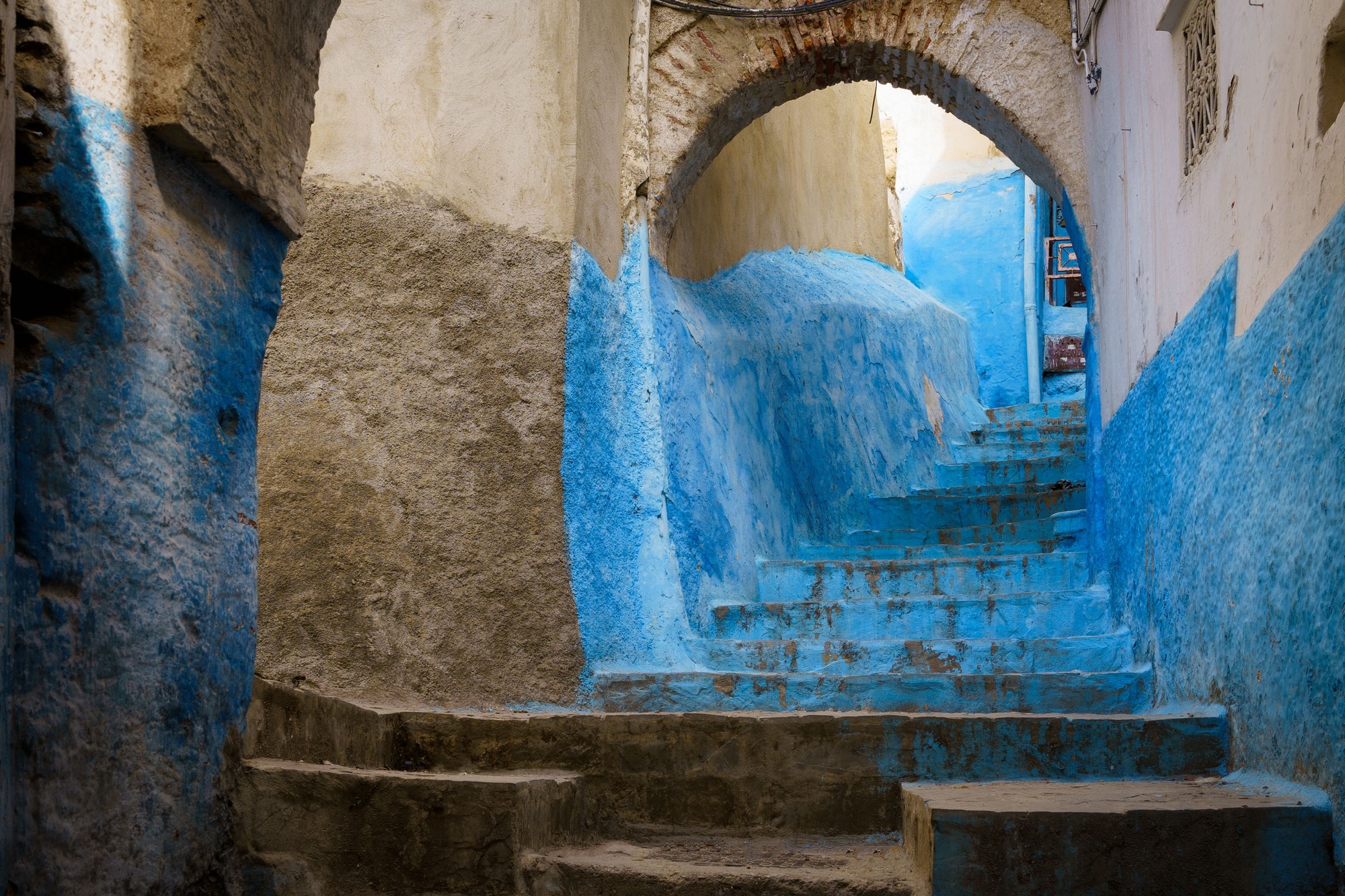 Arch gate with blue stairs on a medieval alley with plant pots in Tetouan, Morroco